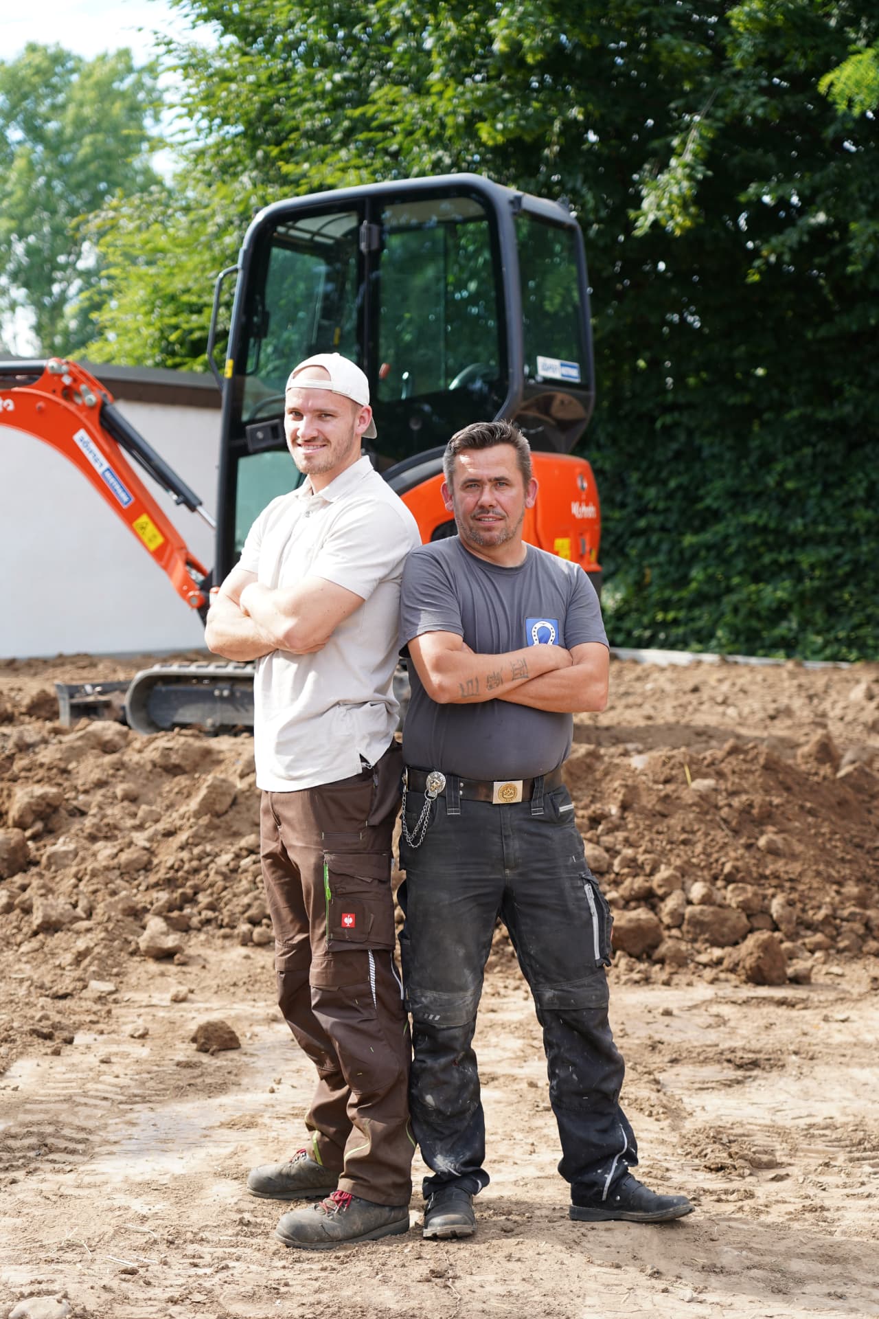 Zwei Mitarbeiter des Brühler Bauhofs vor einem Minibagger auf der Baustelle